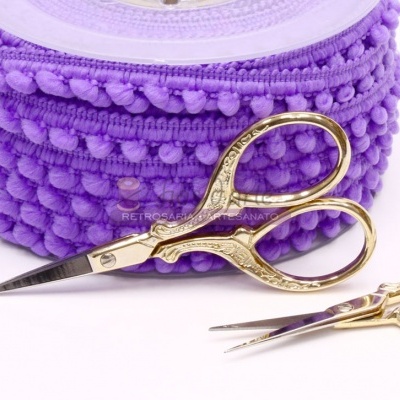 Tesouras douradas ornamentais com fita de pompons roxa ao fundo