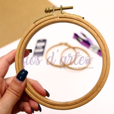 Argolas de bordado em madeira clara com uma segurada pela mão e outra ao fundo