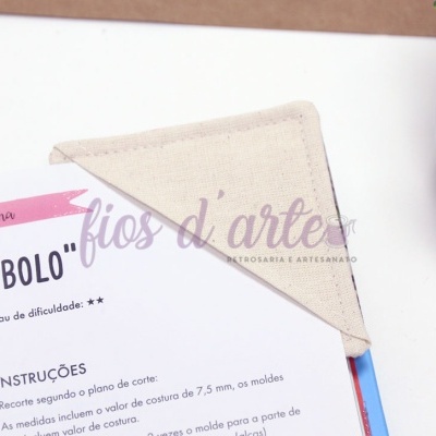 Pano de cozinha triangular bege sobre folha de instruções em português junto a planta em vaso branco