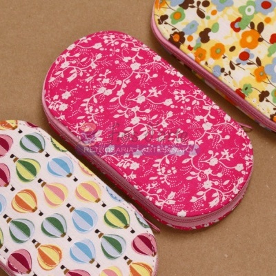 Três estojos coloridos com padrões de balões e flores sobre superfície castanha