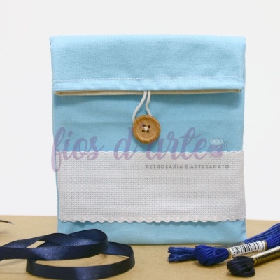 Estojo de tecido azul claro e branco com botão de madeira e fita azul ao lado