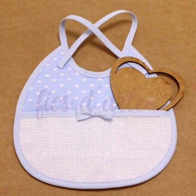 Babete de bebé azul claro com corações brancos e bolso branco quadriculado com laço azul, sobre fundo castanho.
