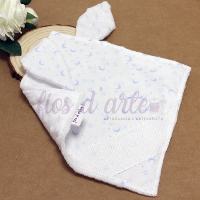 Pano de boca branco com padrão azul de luas e estrelas e textura de bolinhas em relevo.