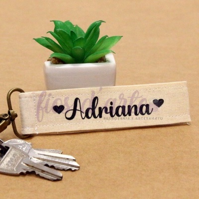Chaveiro de tecido bege com texto e vaso com planta artificial