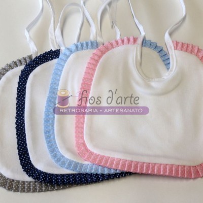 Cinco babetes para bebé com bordas coloridas de bolinhas e fitas brancas num fundo branco.