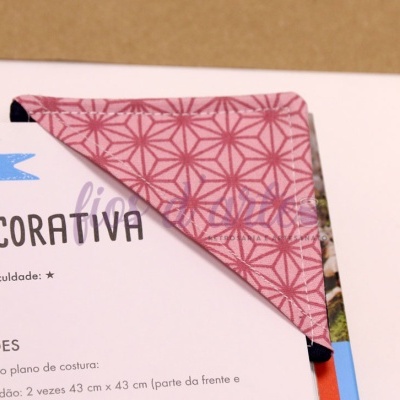 Marcador de livros em tecido rosa com padrão geométrico sobre página de livro em português