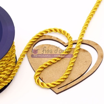 Cordão amarelo sobre molde de coração em madeira clara com fundo branco e objeto azul