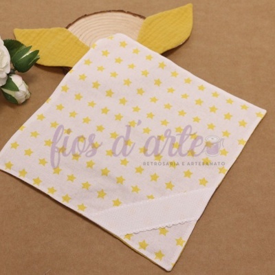 Toalha branca com estrelas amarelas e orelhas amarelas, junto a uma flor branca sobre fundo castanho.