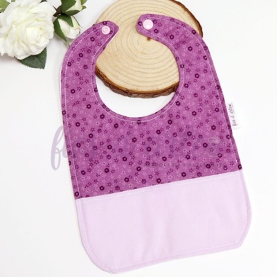 Babete para bebé lilás com padrão de flores roxas e base de madeira