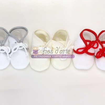 Três pares de sapatinhos para bebé em tecido branco com atilhos de cores diferentes