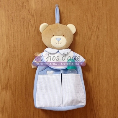 Organizador de tecido azul com ursinho de pelúcia e duas gavetas brancas pendurado numa porta de madeira