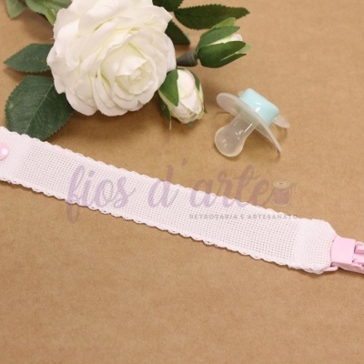 Prendedor de chupeta rosa claro com chupeta azul claro sobre fundo castanho e flores brancas