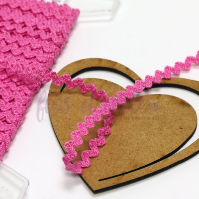 Fita decorativa rosa ondulada sobre molde de coração de madeira.