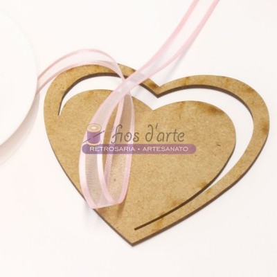 Objeto decorativo de madeira em forma de coração com fita rosa translúcida sobre fundo branco.