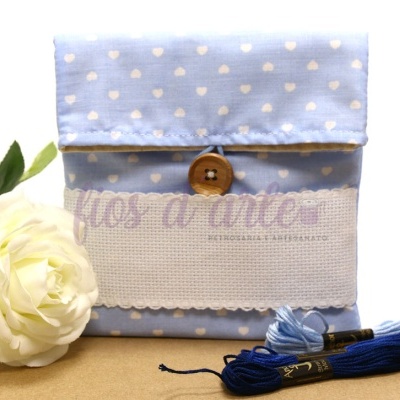 Bolsa pequena azul com corações brancos e botão em madeira, com novelos de fio azul e flor branca ao lado