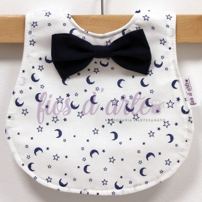 Babete branco com padrão de estrelas e luas azuis e laço azul escuro