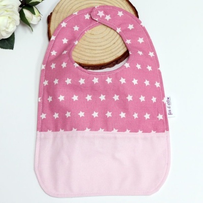 Babete rosa com estrelas brancas sobre base de madeira e flores brancas