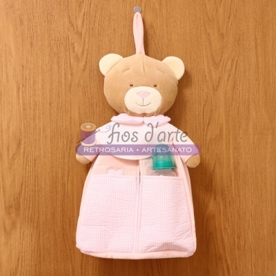 Pelúcia de urso castanho com roupa rosa pendurada numa parede de madeira