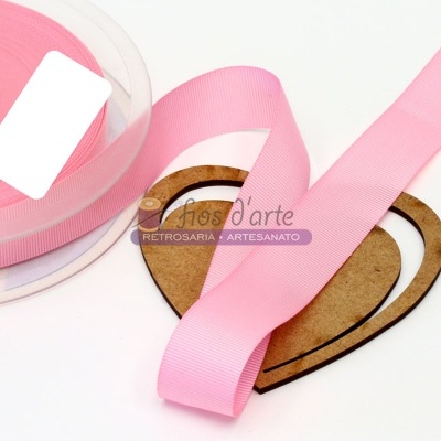 Fita de cetim rosa clara em carretel transparente e fita esticada sobre base de madeira em forma de coração com texto