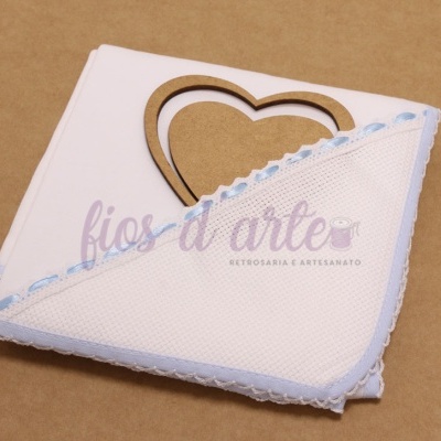Toalha branca com borda azul e renda com coração de madeira ao fundo