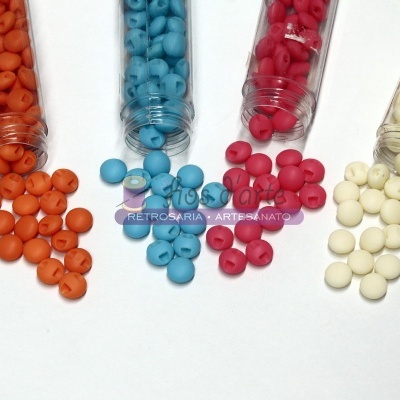 Tubo transparente com contas coloridas laranja, azul, rosa e branco vertendo sobre superfície branca