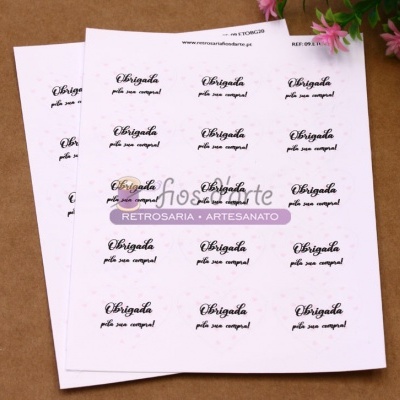 Autocolantes brancos com texto 'Obrigada pela sua compra!' em ambiente artesanal com flores cor-de-rosa