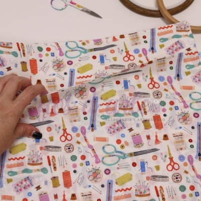 Bolsa de tecido branco com padrão colorido de materiais de costura manuseada por mão feminina.