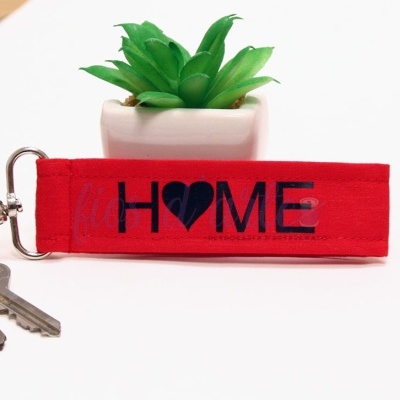 Chaveiro vermelho com texto 'HOME' e planta suculenta verde em vaso branco