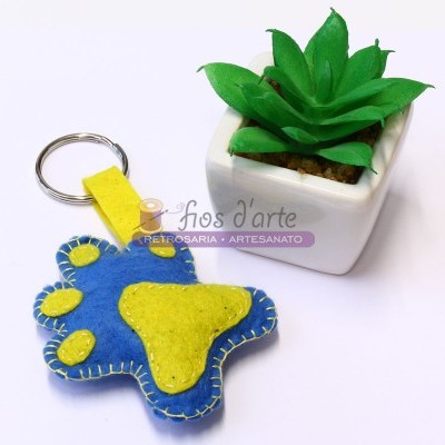 porta-chaves de feltro azul e amarelo em forma de pata junto a planta suculenta em vaso branco