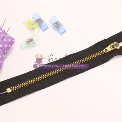 Fecho éclair preto com dentes de metal dourado e almofada de alfinetes roxa com bolinhas brancas