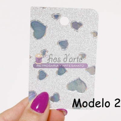 Cartão prateado com corações e texto, segurado por mão com unha roxa