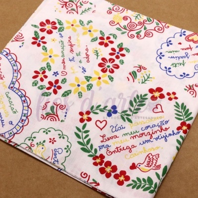 Pano de tecido branco com estampas coloridas de flores e textos em português