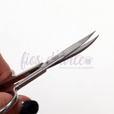 Tesoura de costura curva prateada em mão com unha preta