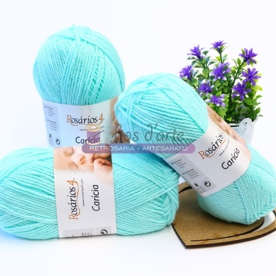 Três novelos de lã azuis Rosários 4 modelo Carícia com planta decorativa ao fundo