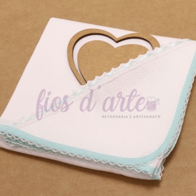 Guardanapo branco com borda azul clara e renda, ornamento de madeira coração ao fundo