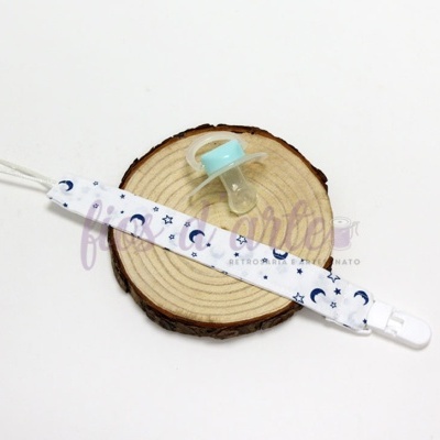 Chupeta azul clara com fita estilizada de luas e estrelas em fundo branco