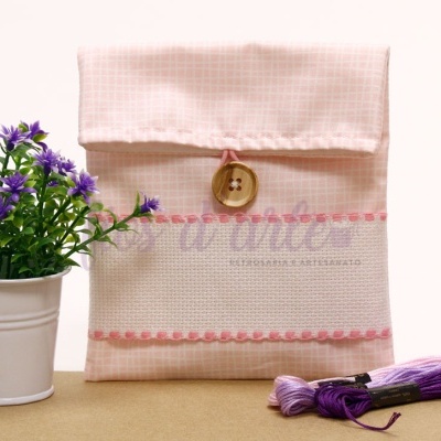 Estojo de tecido rosa com botão de madeira, planta artificial em vaso branco e fios de bordado roxos