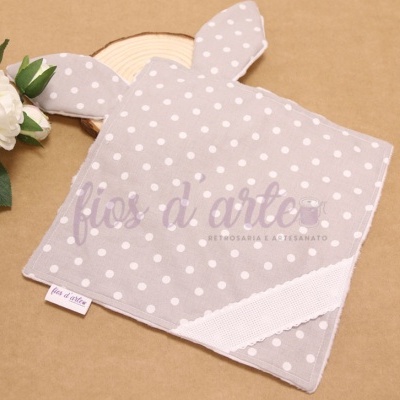 Toalha cinza com bolinhas brancas em forma de coelho com orelhas, sobre fundo castanho claro com flor branca ao lado