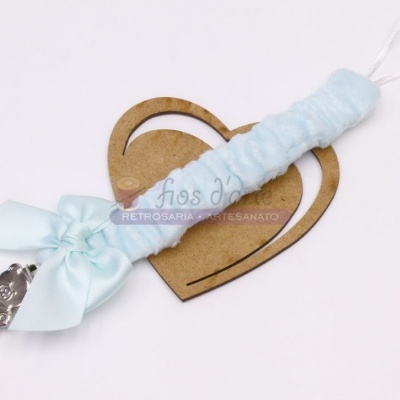 Porta chuchas azul claro com laço e pendente de carrinho prateado sobre base de madeira em forma de coração