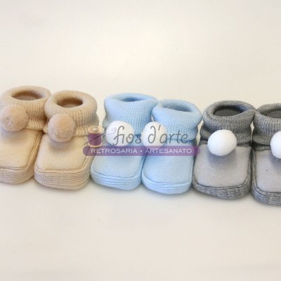 Três pares de sapatinhos de bebé com pompons em bege, azul claro e cinza
