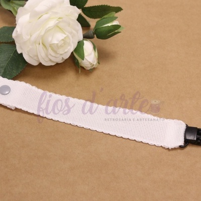 Alça branca de tecido com fecho preto e botão, ao lado de flor branca artificial