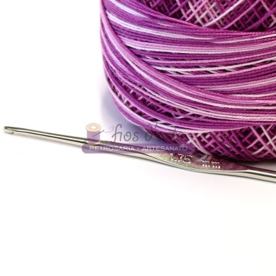 Novelo de fio lilás e agulha de crochê prateada sobre fundo branco