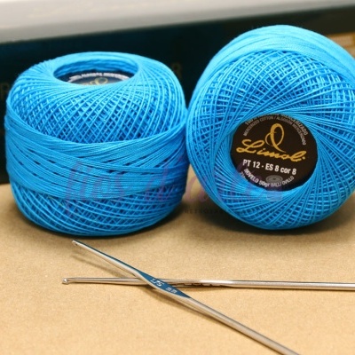 Dois novelos de linha azul clara e agulhas para crochê sobre superfície bege