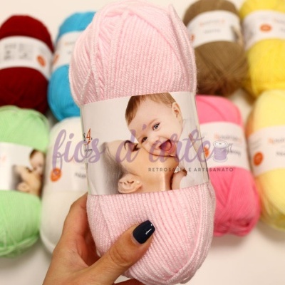 Novelo de lã rosa claro com etiqueta de criança, rodeado por vários novelos de lã coloridos