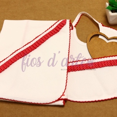 Toalha branca com babete com bordas vermelhas com pontos brancos, planta em vaso branco ao lado