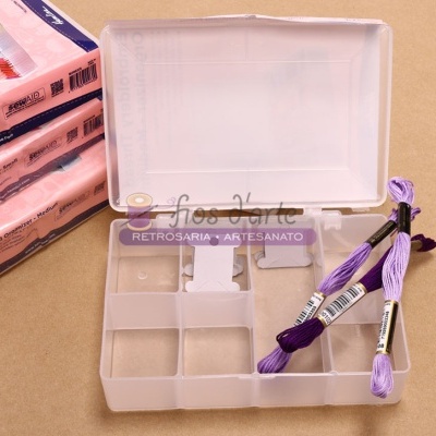 Caixa plástica transparente com linhas de bordado roxas em divisórias à superfície castanha e embalagens cor-de-rosa ao lado