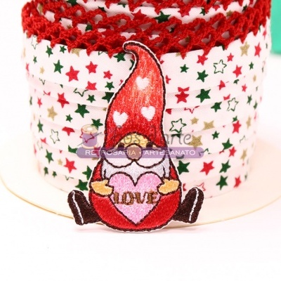 Boneco decorativo de tecido em forma de gnomo com coração, em frente a objeto com padrão de estrelas.