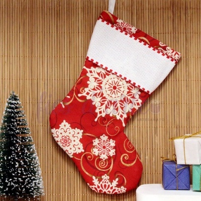 Meia de Natal vermelha com padrões brancos pendurada junto a mini árvore e pequenas caixas de presente