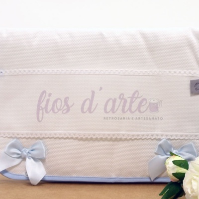 Toalha branca com borda azul e laços, texto 'fios d'arte' e flor branca ao lado