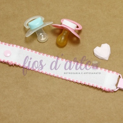 Duas chuchas de bebé com pega azul e rosa e presilha para chucha cor-de-rosa sobre superfície castanha